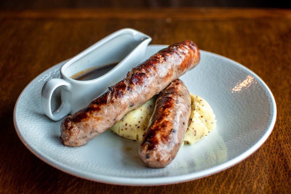 Two large pork sausages on a bed of mash potato, with a jug of onion gravy on the side
